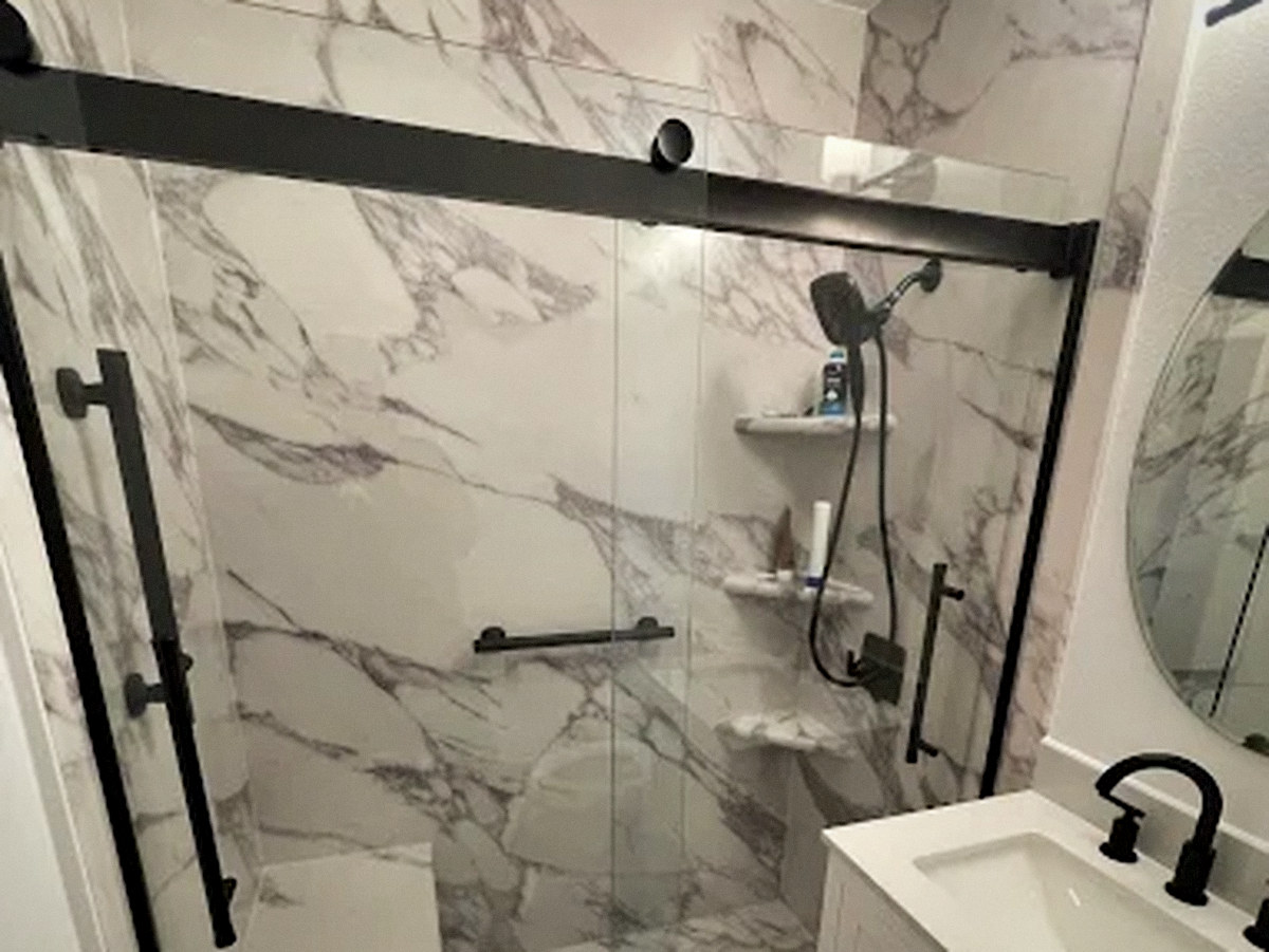 Walk-in shower with marble-look panels, black glass frame and built-in shelves in Englewood, CO