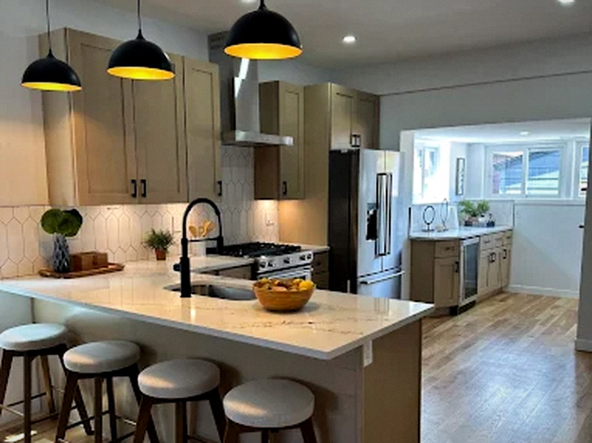 Remodeled kitchen with tan shaker cabinets, a quartz peninsula and black pendant lights in Lakewood, CO